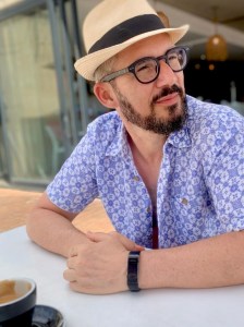 Portrait of Petros Isaakidis, seated, wearing a hat and glasses.